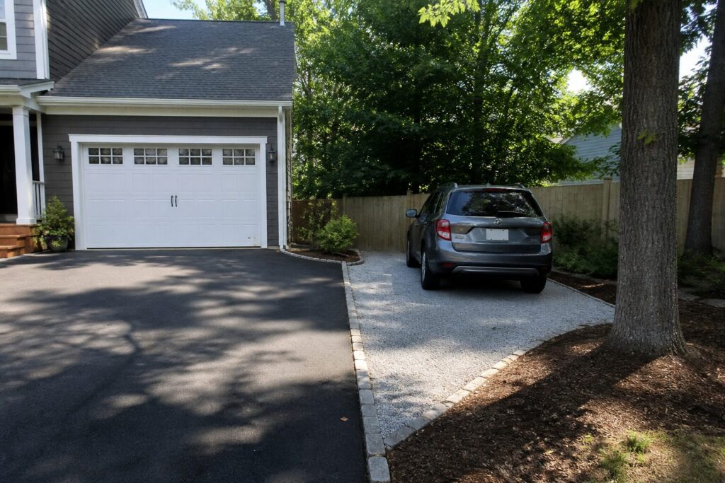 SUV parked on a gravel parking pad beside a paved driveway in a landscaped suburban front yard
